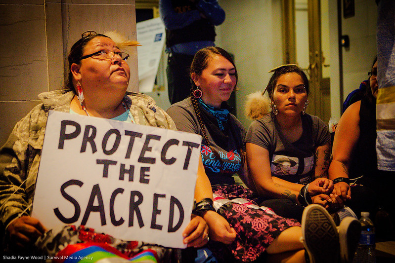 three indigenous women environmental activists hold sign saying "protect the sacred" occupying the BIA in washington dc in october 2021